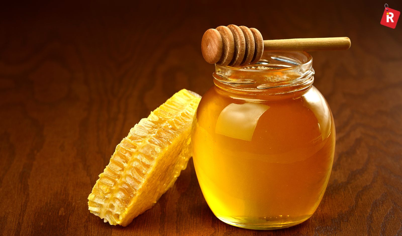 A spoon scooping honey-soaked turmeric from a jar, with a cup of warm water beside it.