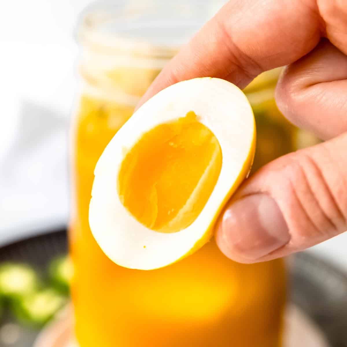 Pouring golden honey over sliced turmeric in a glass jar, honey covering all the turmeric slices.