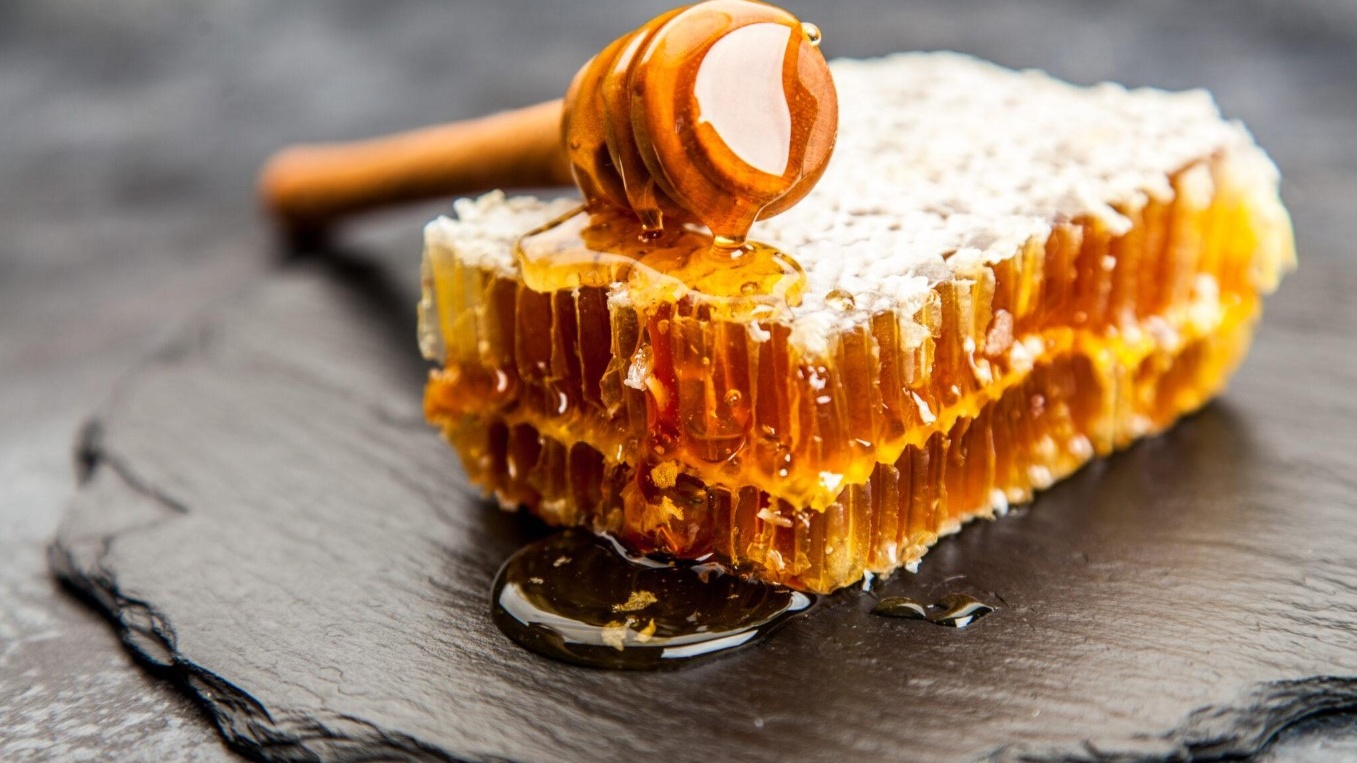 Cận cảnh chai mật ong hoa nhãn Hưng Yên màu vàng óng ánh đặt cạnh cành hoa nhãn nở rộ, thể hiện đặc sản nổi tiếng và mùa thu hoạch mật ong ở Hưng Yên.